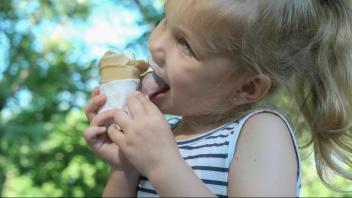 Süßes kleines Mädchen isst draußen Eis. Close-up-Porträt von blonden Mädchen sitzen auf Parkbank und essen Eis. Odessa U