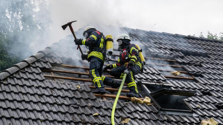 Zwei Feuerwehrmänner auf dem Dach eines brennenden Hauses