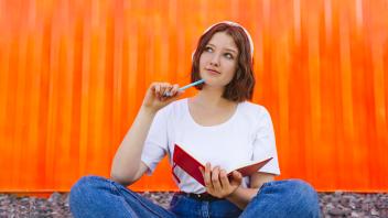 Thoughtful teenage girl with notebook sitting in front of orange cargo container model released, Symbolfoto, IHF01030