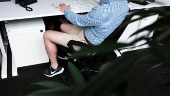 ILLUSTRATION - Ein Mann sitzt mit kurzer Hose an seinem Arbeitsplatz. Beschert uns Corona eine neue Lässigkeit? Foto: Fabian Sommer/dpa