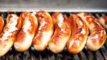 Grillzeit - heiße Würstchen aufgereiht auf dem Holzkohlegrill . Eng nebeneinander liegende gegrillte Bratwürste auf dem