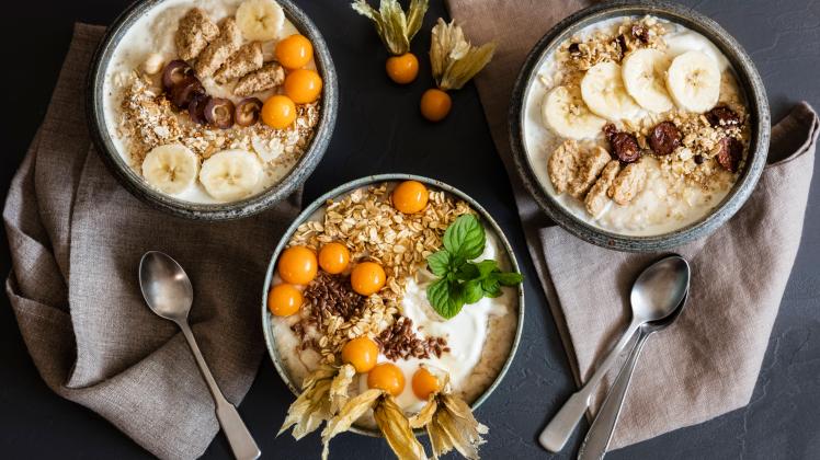 Three bowls of porridge with oats, flax seed, winter cherries and bananas EVGF03768