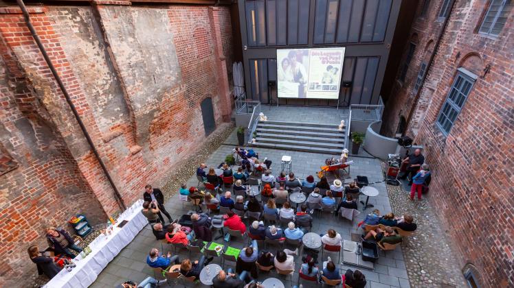 Zuschauer sitzen vor einer Kinoleinwand im Hof eines Museums