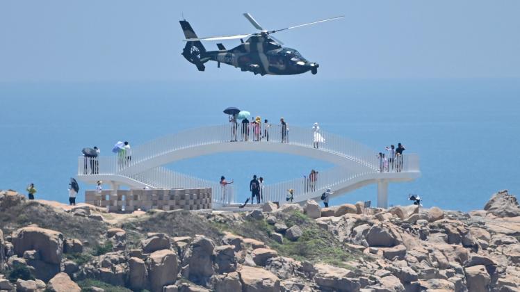 Tourists look on as a Chinese military helicopter flies past Pingtan island, one of mainland China&apos;s closest point from Taiwan, in Fujian province on August 4, 2022, ahead of massive military drills off Taiwan following US House Speaker Nancy Pelosi&apos;s visit to the self-ruled island. - China is due on August 4 to kick off its largest-ever military exercises encircling Taiwan, in a show of force straddling vital international shipping lanes following a visit to the self-ruled island by US House Speaker Nancy Pelosi. (Photo by Hector RETAMAL / AFP)