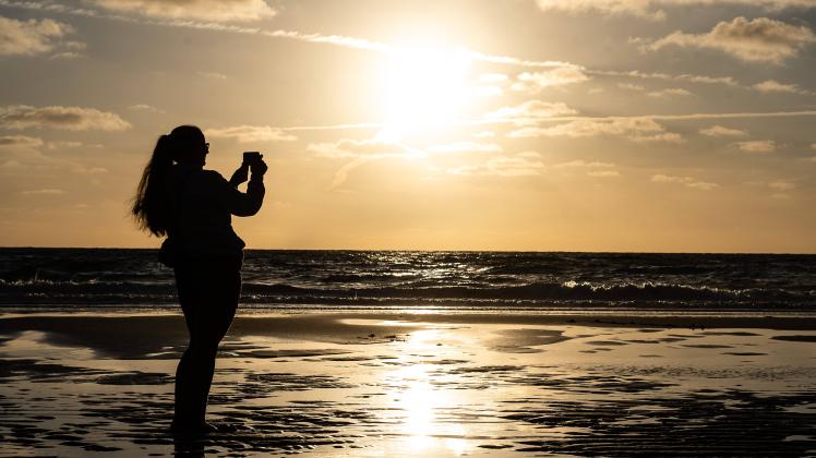 Sommer auf der Insel Sylt 01.08.2022, Wenningstedt --- Eine Frau fotografiert den Sonnenuntergang auf der Nordseeinsel S