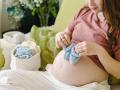 Pregnant woman holding crochet baby booties on stomach at home model released, Symbolfoto property released, SEAF00968