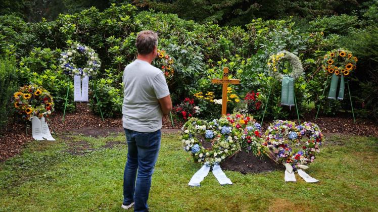 Ein Mann steht in stillem Gedenken an dem mit Kränzen und Blumen geschmückten schlichten Grab der Fußballlegende Uwe Seeler. Foto: Christian Charisius/dpa