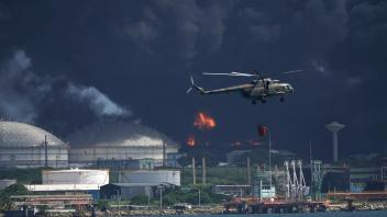 Ein mit Wasser beladener Hubschrauber fliegt über die Supertanker-Basis Matanzas, von der dunkler Rauch und Flammen aufsteigen. Foto: Ramon Espinosa/AP/dpa
