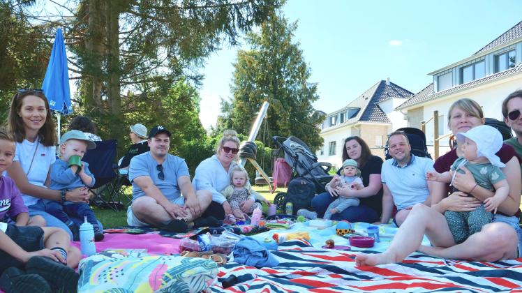 Nachbarschaft einmal anders: junge Familien sitzen im Schatten auf Decken zusammen und essen und trinken.