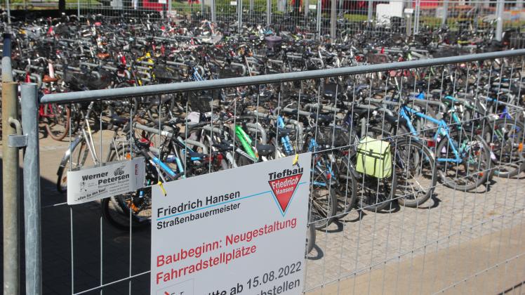 Fahrräder stehen auf dem Abstellplatz am Niebüller Bahnhof. Ein Schild an einem Bauzaun weist seit 4. August 2022 auf bevorstehende Bauarbeiten hin, die am 15. August 2022 beginnen sollen.