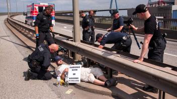 Polizisten versuchen auf der Köhlbrandbrücke zwei mit einem Eisenrohr miteinander verbundene Klimaaktivisten zu lösen. Foto: Daniel Bockwoldt/dpa