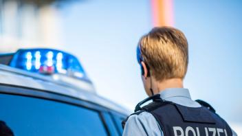 ILLUSTRATION - Eine Polizistin steht vor einem Streifenwagen. Foto: David Inderlied/dpa/Illustration