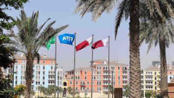ARCHIV - Flaggen in den Farben Katars und eine Fifa-Flagge wehen unter Palmen. Foto: Christian Charisius/dpa