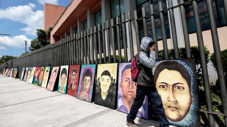 (FILES) In this file photo taken on September 24, 2015, a student walks past portraits of some of the 43 missing students of the rural teacher college of Ayotzinapa placed by fellow students in front of the Congress of the state of Guerrero in Chilpancingo, Mexico, after a march from the school. - Mexican soldiers bear some responsibility, for their actions or omissions, in the disappearance of 43 students from the Ayotzinapa normal school in 2014, according to a report by a government commission released on August 18, 2022. (Photo by Pedro PARDO / AFP)