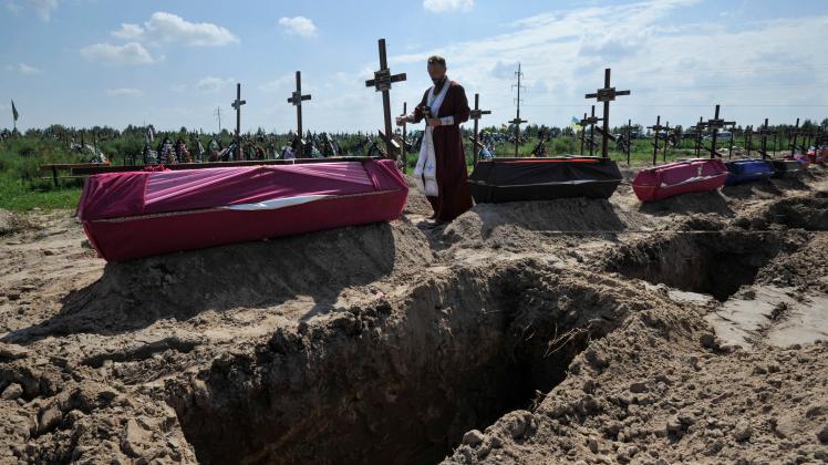 August 17, 2022, Bucha, Ukraine: An Orthodox priest reads a prayer at the graves of unidentified civilians who were kil
