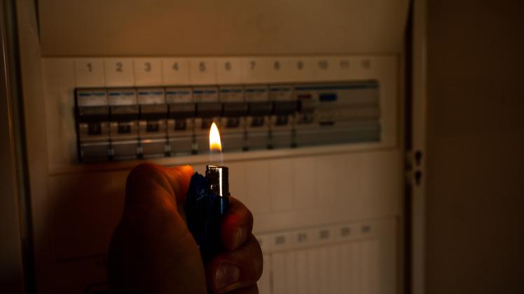 21 August 2022: Man with lighter in darkness examines fuse box o home during power outage. Power failure, no power, blac