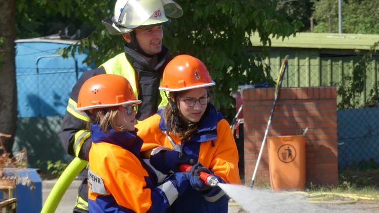 Mili (10) und Sofia (11) bereiten die Löschwasserleitung vor bzw. löschen das Feuer unter Aufsicht ihres Ausbilders Warim Westphal.