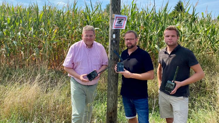Schilder weisen darauf hin, dass der Mais videoüberwacht wird: Stemwedes Bürgermeister Kai Abruszat (li.) ließ sich von den beiden Landwirten Daniel (Mitte) und Marvin Schlechte die Wildkameras zeigen und die Problematik erklären. 
