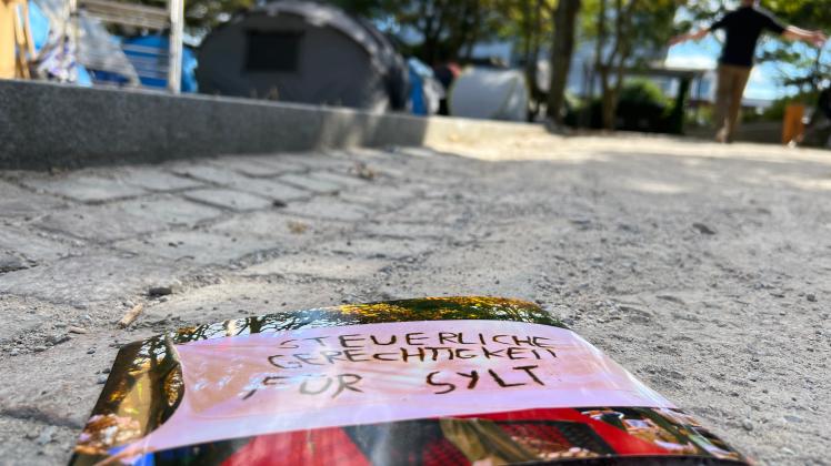„Steuerliche Gerechtigkeit für Sylt“, steht auf einem Foto, das auf dem Boden neben dem Punk-Protestcamp auf Sylt liegt. 