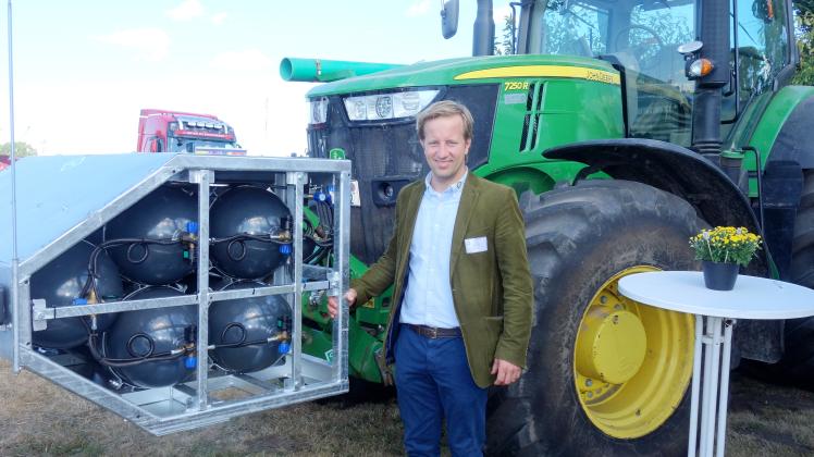 Lohnunternehmer-Chef Niels Schäfer vor einem umgerüstet Trecker. In den Tanks neben ihm befindet sich das verflüssigte Biomethan.        