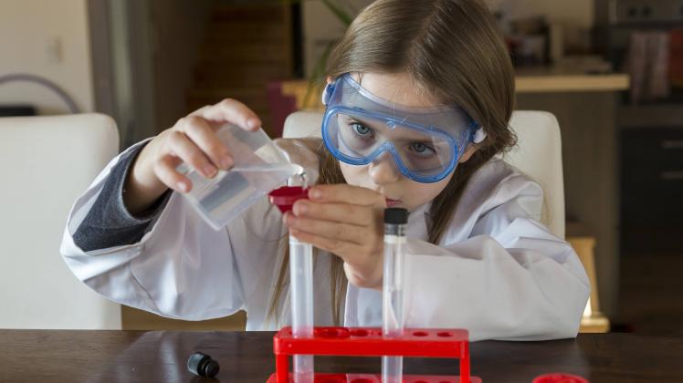 Girl wearing work coat and safety glasses using chemistry set at home model released Symbolfoto PUBL