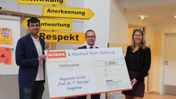 Schulleiter Arne Helmrich (l) nimmt den Scheck der Norma-Stiftung von Tobias Poggendorf (m) und Annett Naborowski entgegen