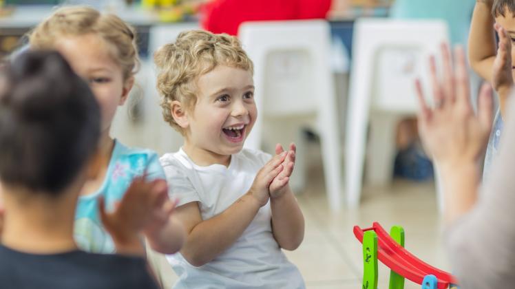 Happy children and pre school teacher clapping hands in kindergarten model released Symbolfoto prope