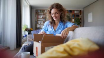 Woman opening box while sitting on sofa at home model released Symbolfoto property released RBF07952