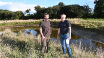 Grundstücksbesitzer Sönke Bosholm (links) und Landschaftspfleger Thomas Hinrichs (Ecodots) an einem 2021 angelegten Gewässer. Hier sollen sich Amphibien und andere Tiere ansiedeln. Das ausgehobene Erdreich wurde zum Bau eines Knicks gleich nebenan verwendet. 