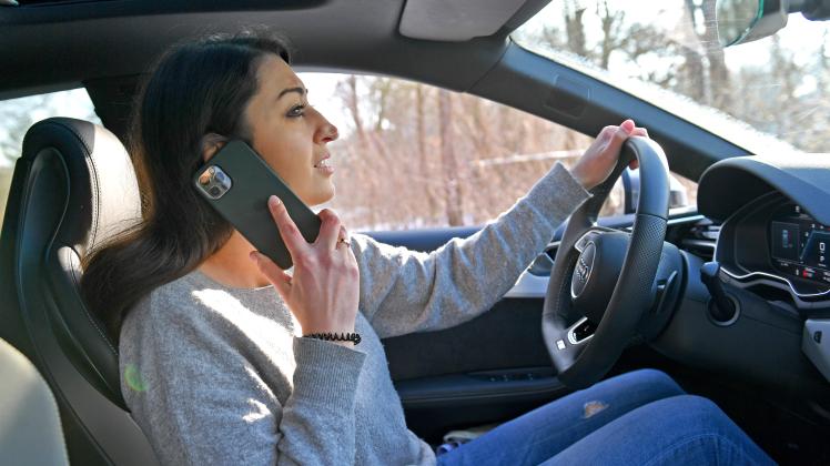 Themenbild Frau mit Smartphone am Steuer eines PKW. Eine junge Frau am Steuer eines PKW,Auto-telefoniert mit ihrem Smart