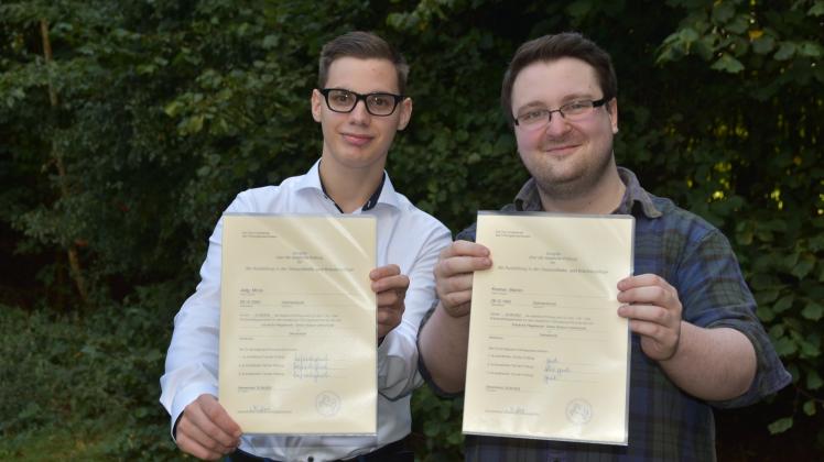 Die Auszubildenden Mirco Jielg (von links) und Marvin Kremer halten nach der bestandenen letzten Prüfung stolz ihre Examensurkunden in die Kamera.