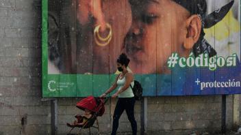 A woman and her baby walk past a banner in favor of the new Family Code referendum under the rain in Havana, on September 23, 2022. - Cubans will vote on Sunday in a referendum on whether to allow same-sex marriage and surrogate pregnancies, which experts say could turn into an opportunity to voice opposition against the government. (Photo by YAMIL LAGE / AFP)