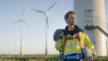 Technician standing at a wind farm with climbing equipment model released Symbolfoto PUBLICATIONxINx