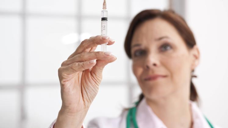 Ärztin hält prüfend eine Spritze in der Hand  - MODEL RELEASED