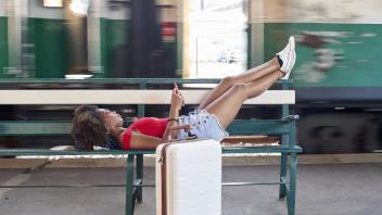 Woman with suitcase lying on a bench at the train station model released Symbolfoto property release