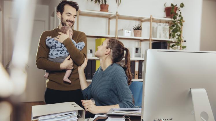 Smiling mother at desk looking at father holding baby in home office model released Symbolfoto prope