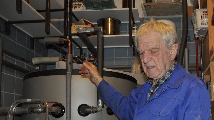 Ewald Sülter an seinem Pufferspeicher. In der Hand hält er einen Zwangsmischer, der künftig für die richtige Wassertemperatur sorgen soll.