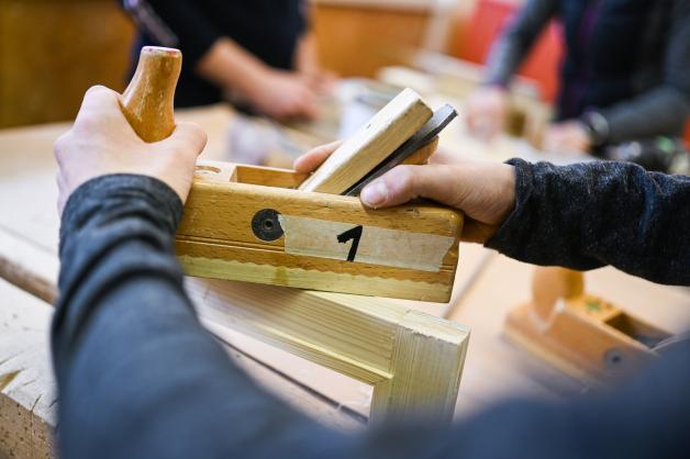 Ein Auszubildender im Schreiner-Handwerk arbeitet mit dem Hobel an seinem Werkstück. Ein Auszubildender im Schreiner-Handwerk arbeitet mit dem Hobel an seinem Werkstück.