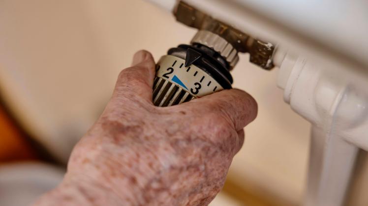 Hand einer Seniorin mit Altersflecken auf dem Thermostat einer Heizung, Köln, Nordrhein-Westfalen, Deutschland, Europa *