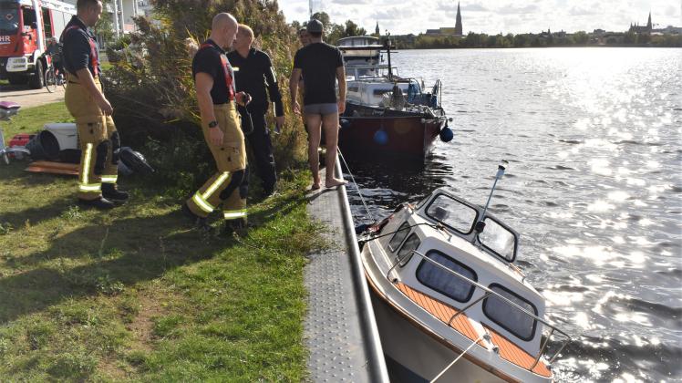 Einsatzkräfte von Polizei und Feuerwehr versuchen, das mit Schlagseite an der Kaikante vertäute Sportboot vor dem Sinken zu bewahren.