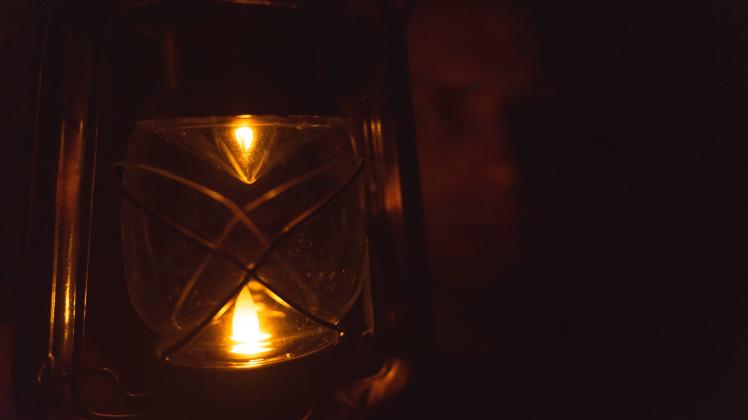 Bavaria, Germany - 25 September 2022: Man with lantern in dark room, power failure at home. Light and power in the apart