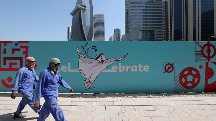 Workers walk past a billboard showing an illustration of the Qatar 2022 FIFA World Cup mascot "La&apos;eeb" in the Qatari capital Doha on October 13, 2022, ahead of the 22nd edition of the international football competition. - The first world cup to take place in the Arab world, is scheduled to kick off on November 20, with the host nation Qatar taking on Ecuador. (Photo by GIUSEPPE CACACE / AFP)