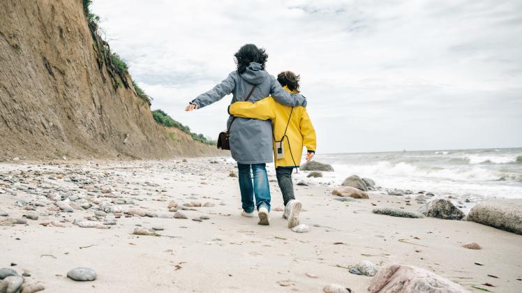 little girl in yellow raincoat walking embraced with mother on stone beach