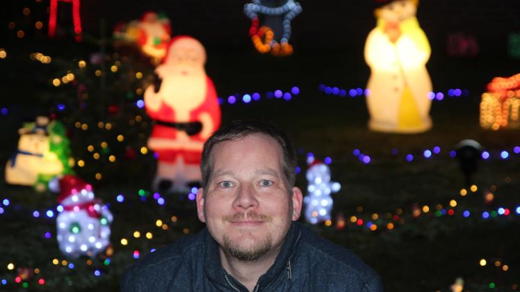 Christian Brodersen aus Maasbüll (Gemeinde Risum-Lindholm) kniet am 15. Dezember 2021 im Vorgarten seines Wohnhauses vor beleuchteter Weihnachtsdeko.