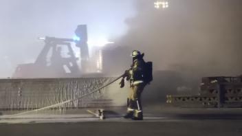 Ein Feuerwehrmann löscht den in Brand geratenen Holzstapel.