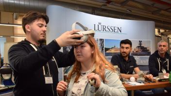 Am Stand der Schacht-Audorfer Lürssen-Werft setzt Azubi Masar Nulin der Schülerin Merle Petersen eine VR-Brille auf.