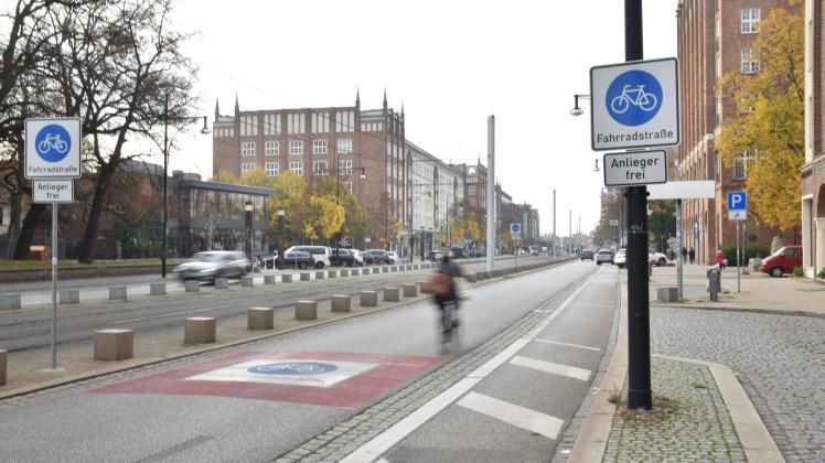 Lange Straße bei hoher Belichtung mit einem verschwomenem Fahrradfahrer und den Schildern für die Fahrradstraße