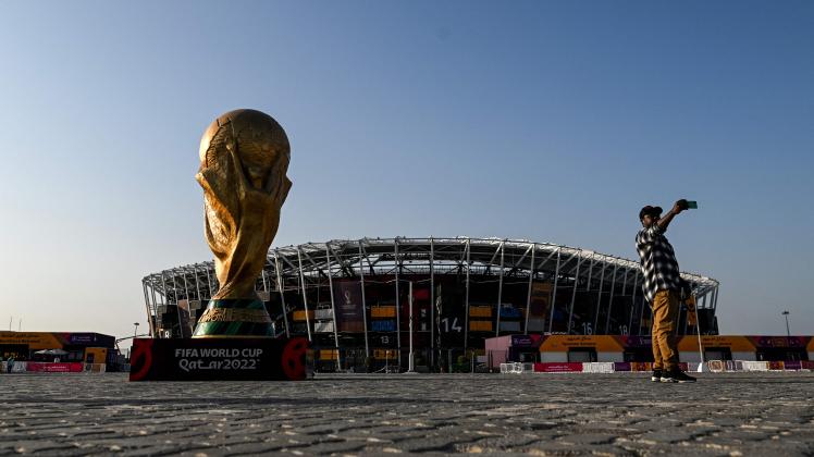 TOPSHOT - A man takes a picture in front of a replica of the World Cup trophy outside the Stadium 974 in Doha on November 15, 2022, ahead of the Qatar 2022 World Cup football tournament. (Photo by Kirill KUDRYAVTSEV / AFP)