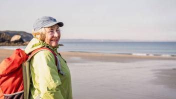 Happy senior woman with backpack standing at beach model released, Symbolfoto, UUF27189