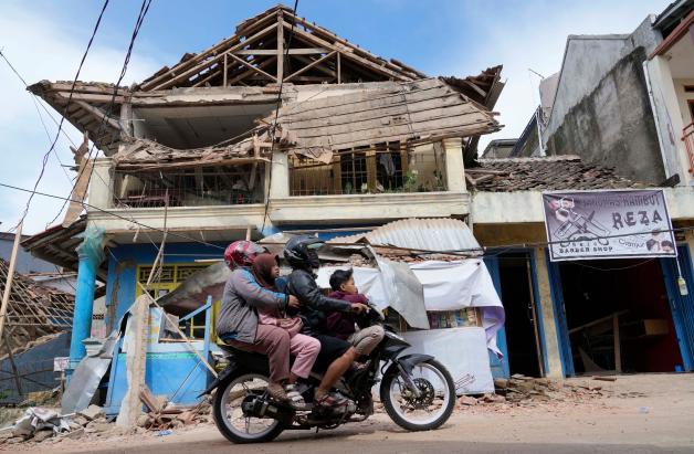 Menschen fahren auf einem Motorrad an einem Gebäude vorbei, das bei dem Erdbeben am Montag beschädigt wurde.